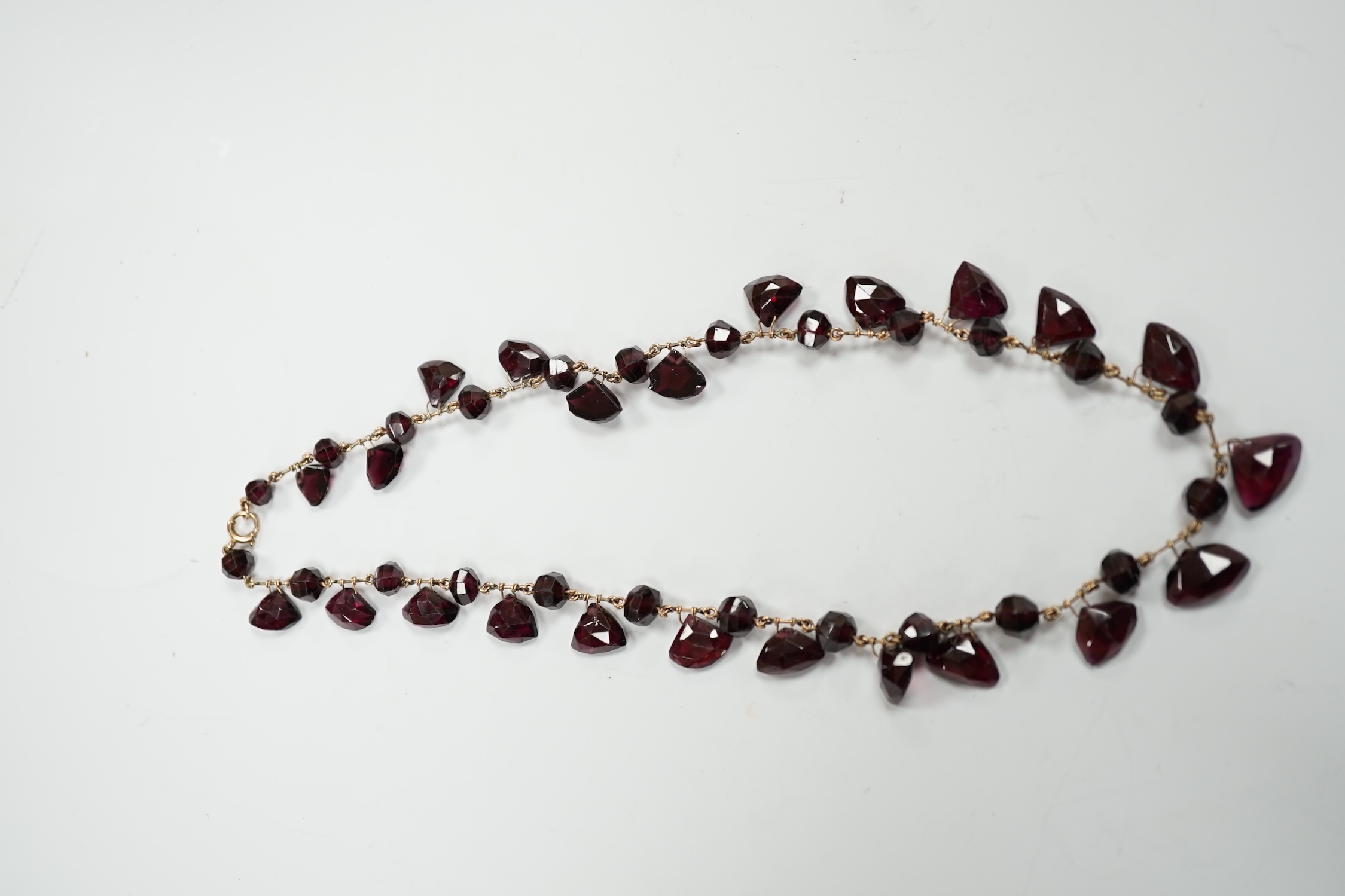 A Victorian yellow metal (test as 9ct) and garnet drop fringe necklace, set with faceted circular and pebble cut stones, 38cm, gross weight 32.6 grams.